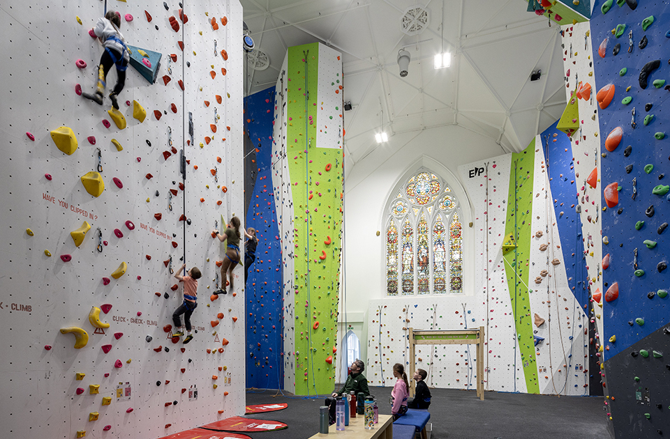Above Adventure climbing centre within former church. Children on climbing wall. Stained glass windows in background.